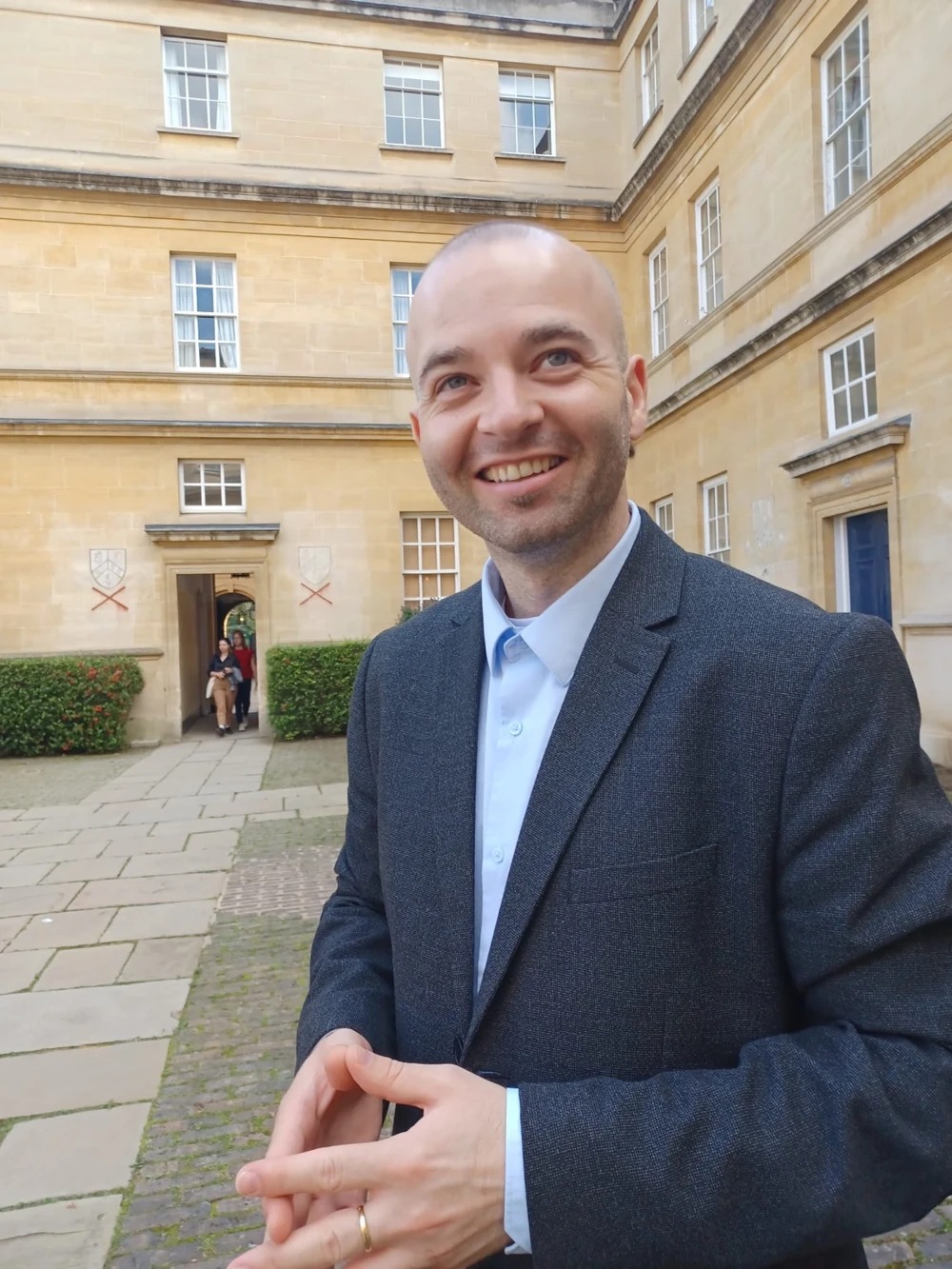 Fabjan Pepaj smiling in a courtyard, wearing a dark blazer